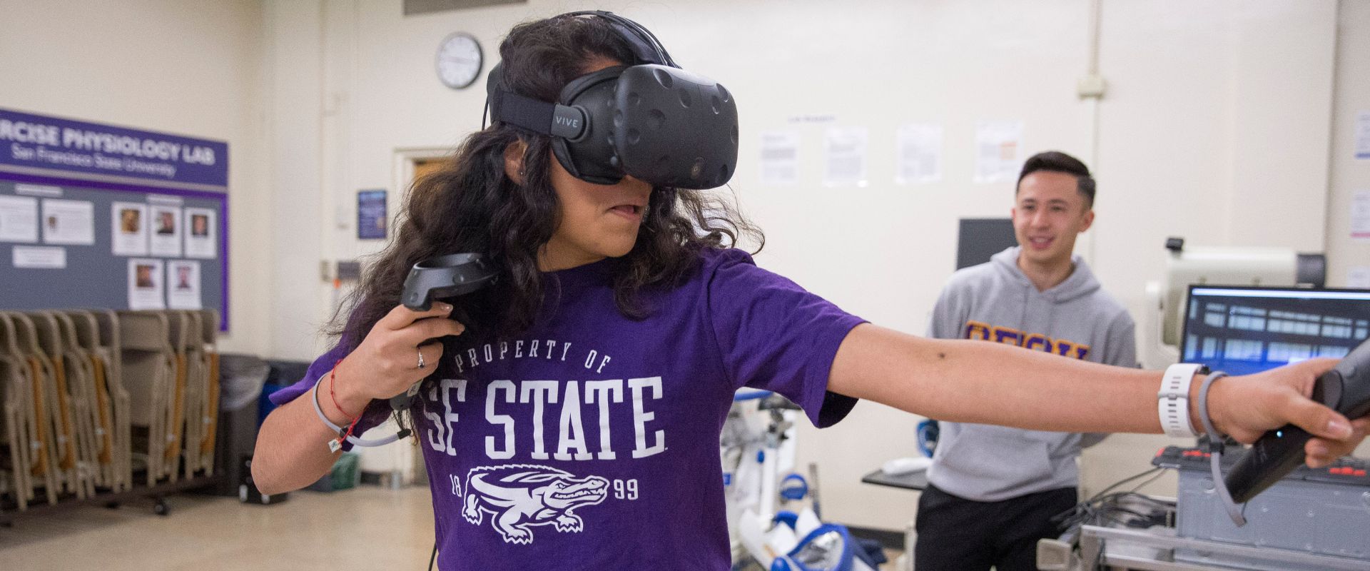 Student exercises in virtual reality while another watches