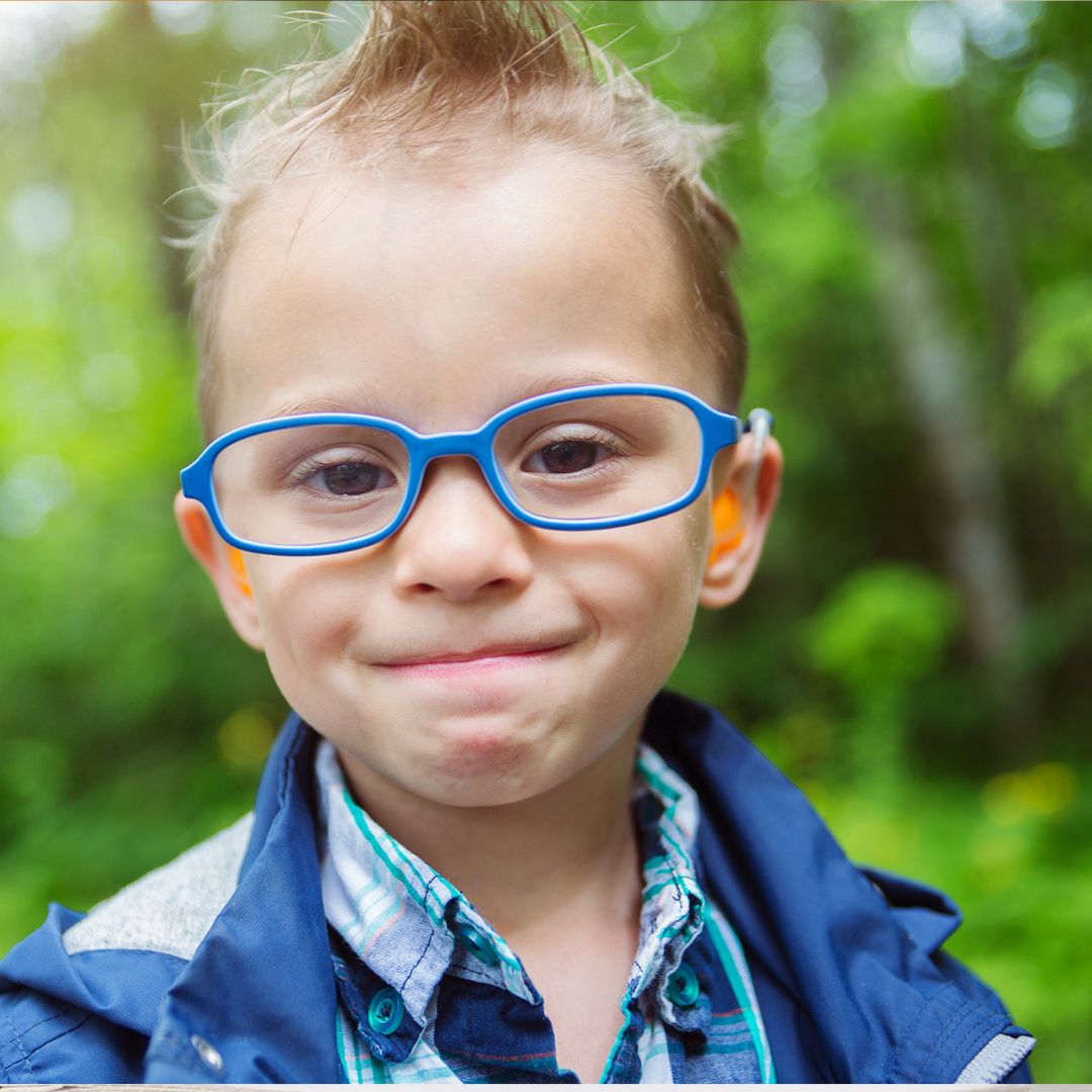 Young child wearing blue glasses and a hearing aid