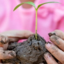 Child in pink shirt holds a globe of mud with a sprout coming out