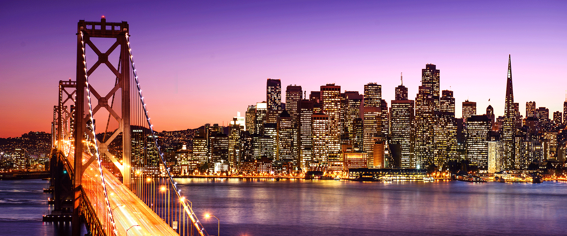 A iew of the Bay Bridge and Downtown San Francisco with a purple sunset