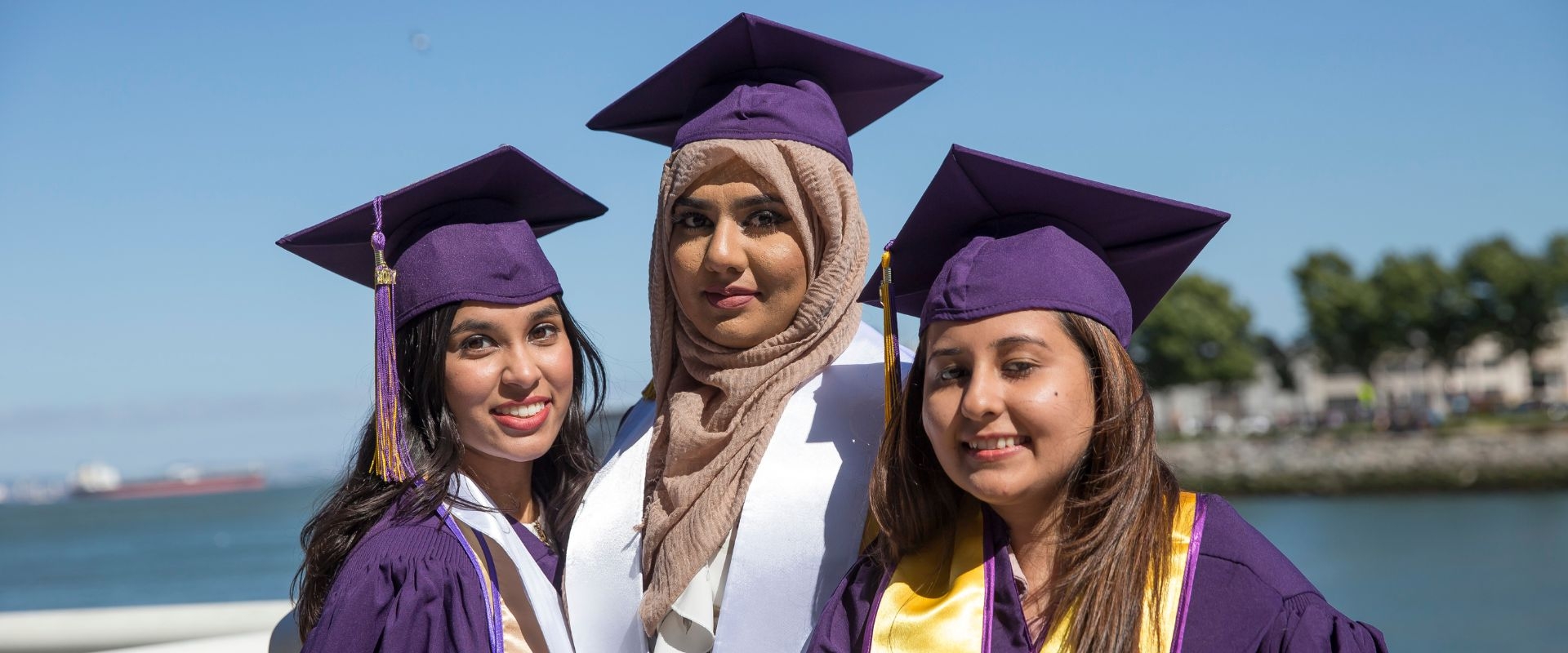 Three graduates in regalia on the beach