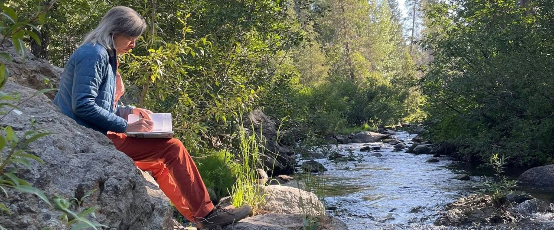 Student studies by a stream in the Sierra
